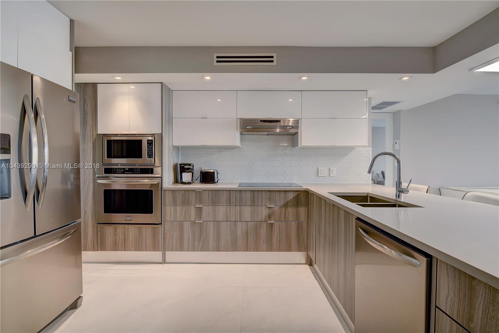 Soft brown and white color palette sets the tone for this open, contemporary kitchen. Sleek cabinets pair with chic quartz countertops, and stainless steel pro-quality appliances complement the modern aesthetic