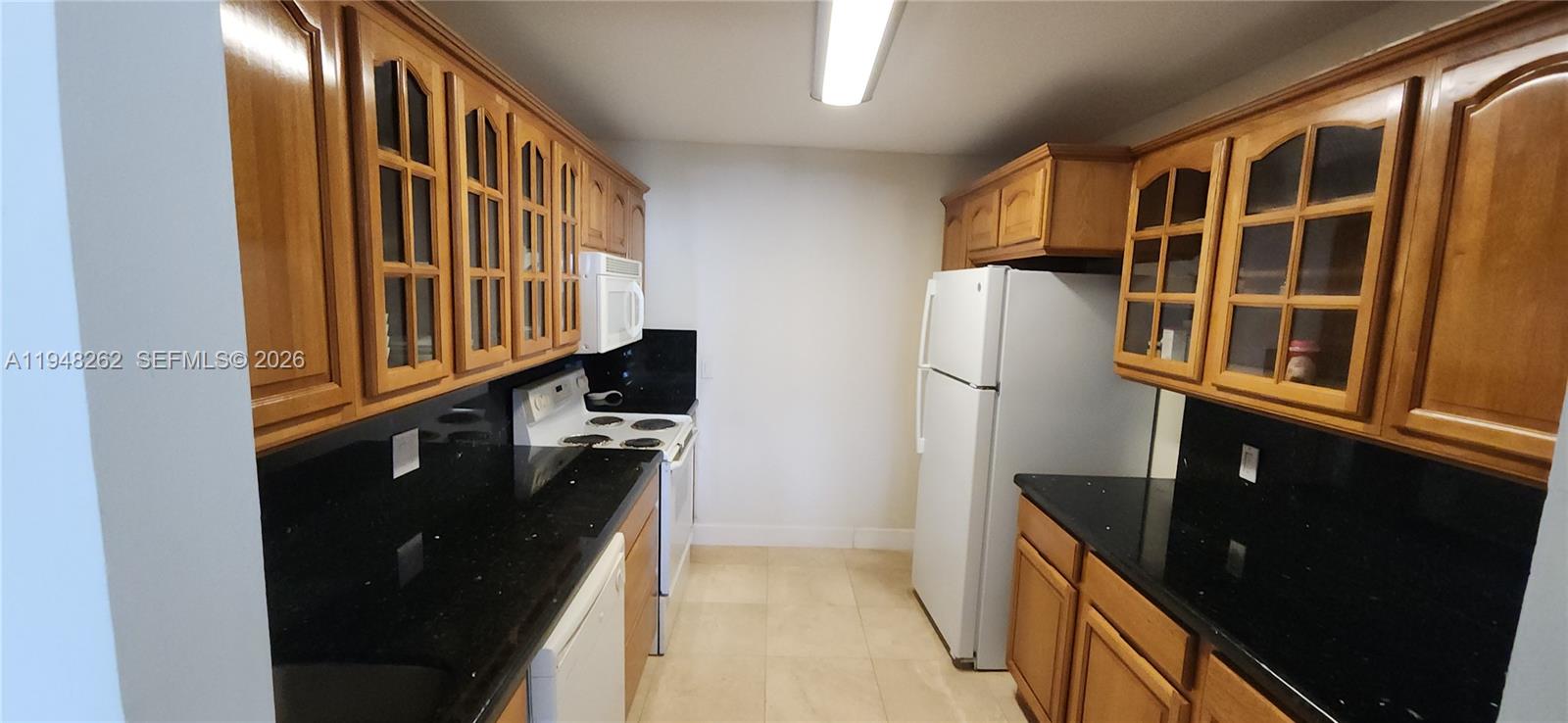 Photo of 2101 Ocean Dr  #2608, Hollywood, Florida, 33019 - very bright area..This image shows a galley-style kitchen featuring traditional wooden cabinetry with a medium-oak finish. The upper cabinets include several units with glass-paneled doors, adding a decorative touch to the storage space.