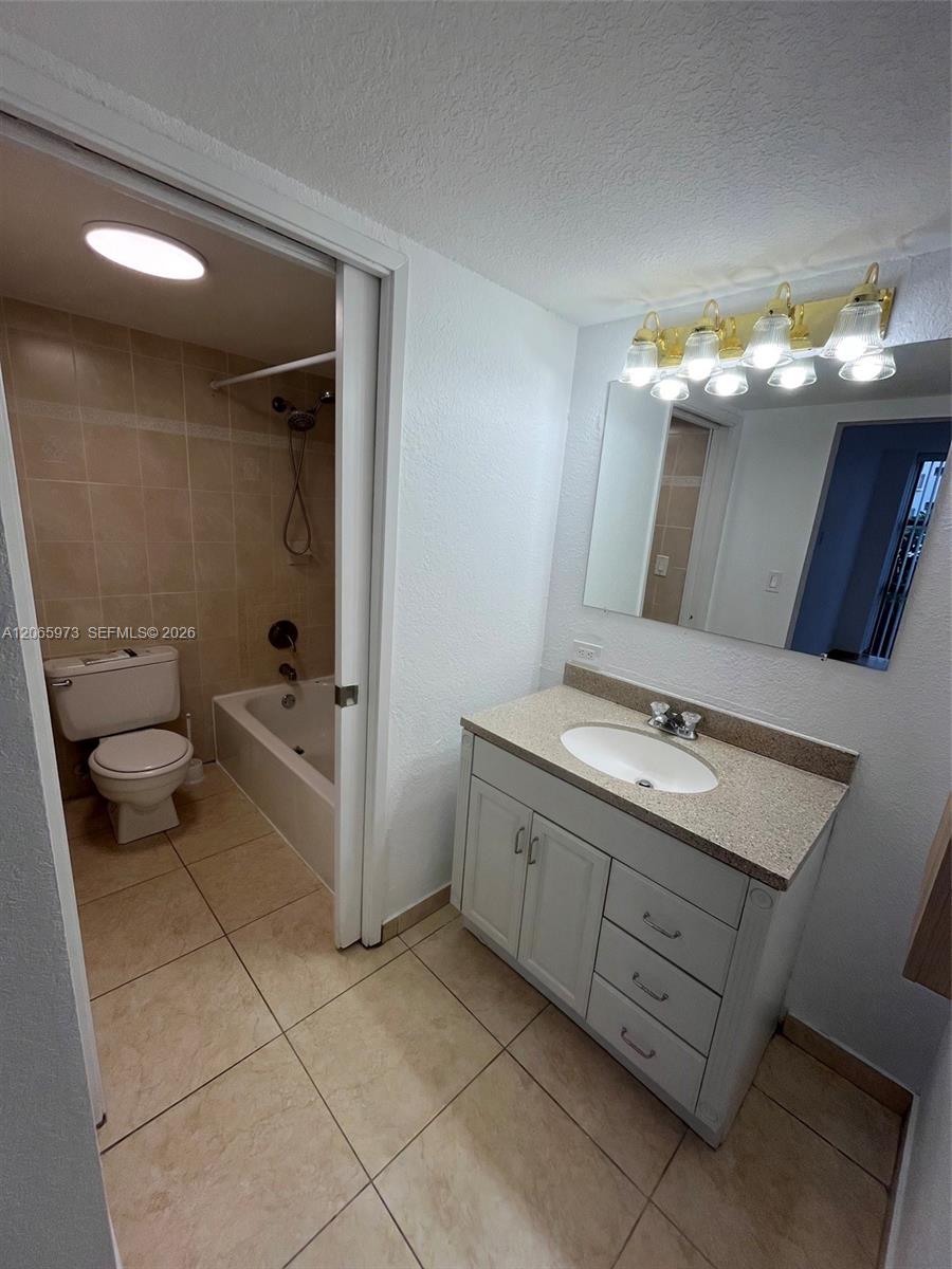 Bathroom featuring a vanity with shaker-style cabinetry, stone-composite countertop with an integrated basin, ceramic tile flooring, and a tub-shower combination with tiled surround
