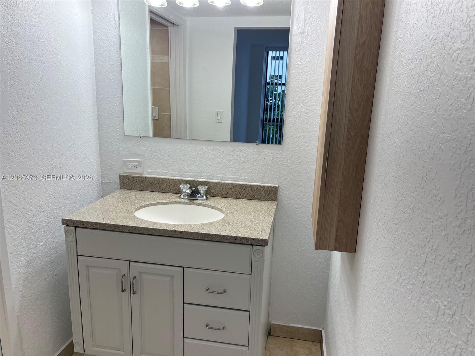Vanity featuring a stone-composite countertop with an integrated oval sink, paired with a flat-panel wooden wall cabinet, a large frameless mirror, and overhead lighting