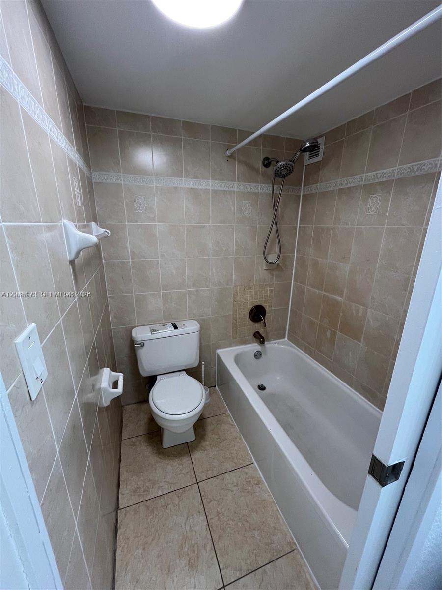 Full-height wall tile with decorative accent border, ceramic floor tiling, porcelain bathtub with integrated shower head, and dual-flush toilet