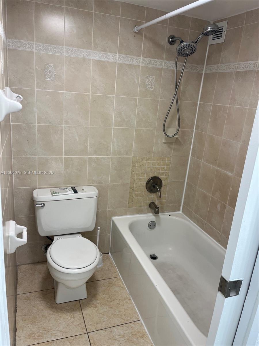 Bathroom featuring neutral tile wall surround with decorative accent inlay, porcelain soaking tub, handheld shower fixture, and ceramic tile flooring