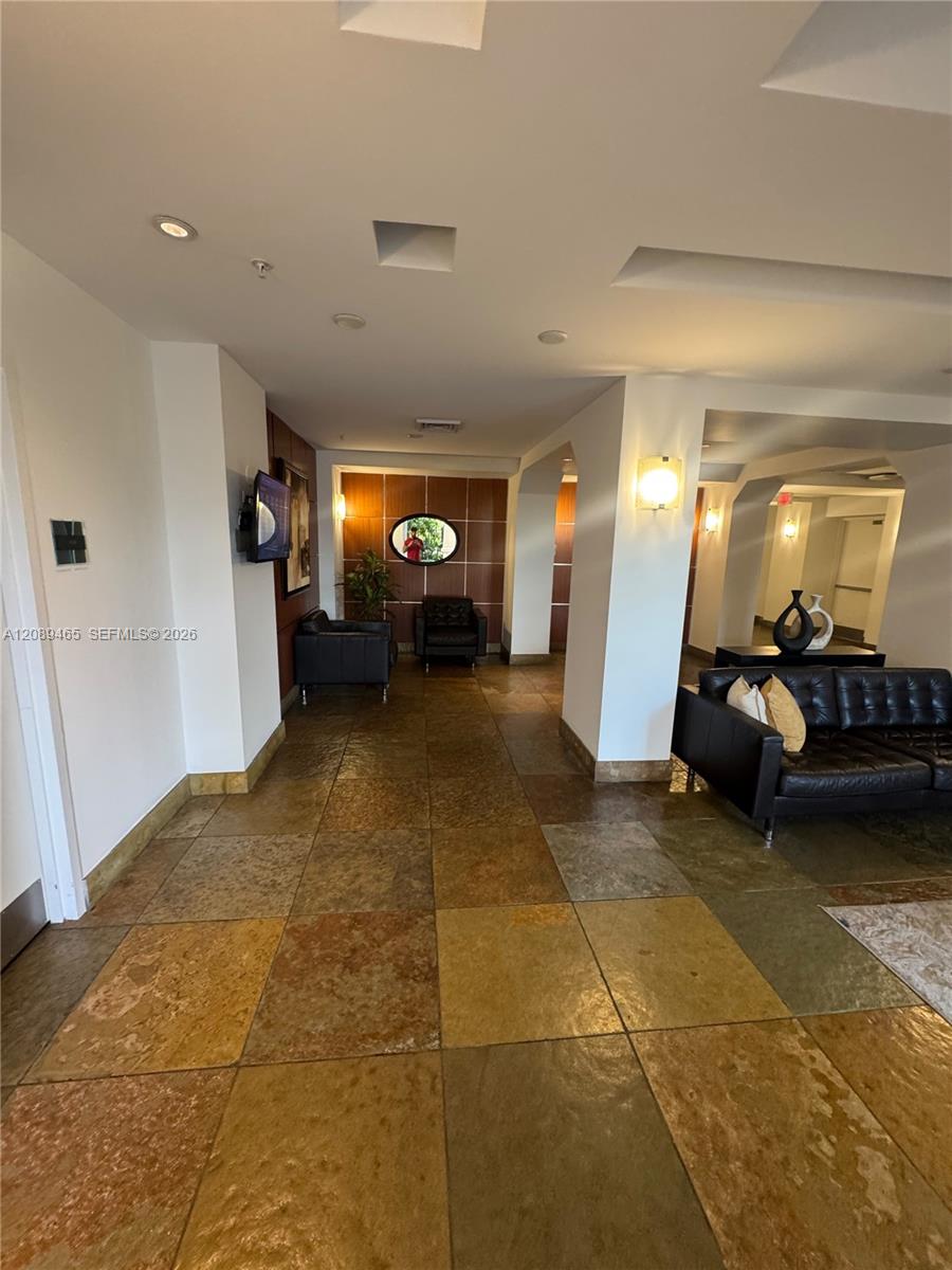 Large-format stone tile flooring, recessed ceiling lighting, wall-mounted sconces, and wood-paneled accent wall/