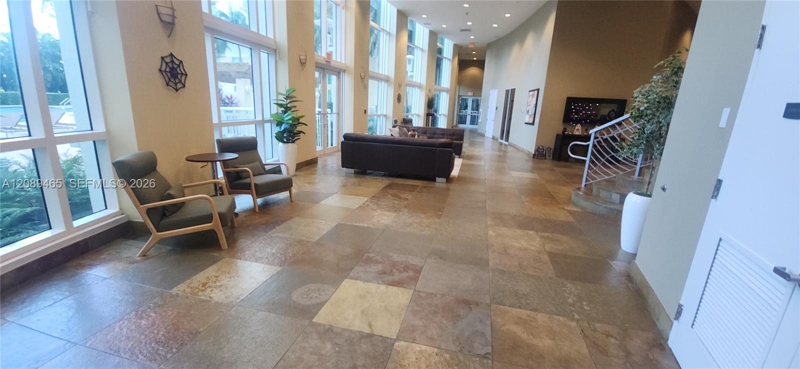 Large-format stone tile flooring, multi-tiered tray ceiling with recessed lighting, and wall-mounted sconces
