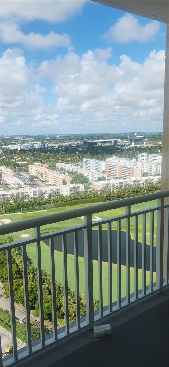 Elevated balcony with a white metal railing overlooking a golf course, water feature, and urban landscape