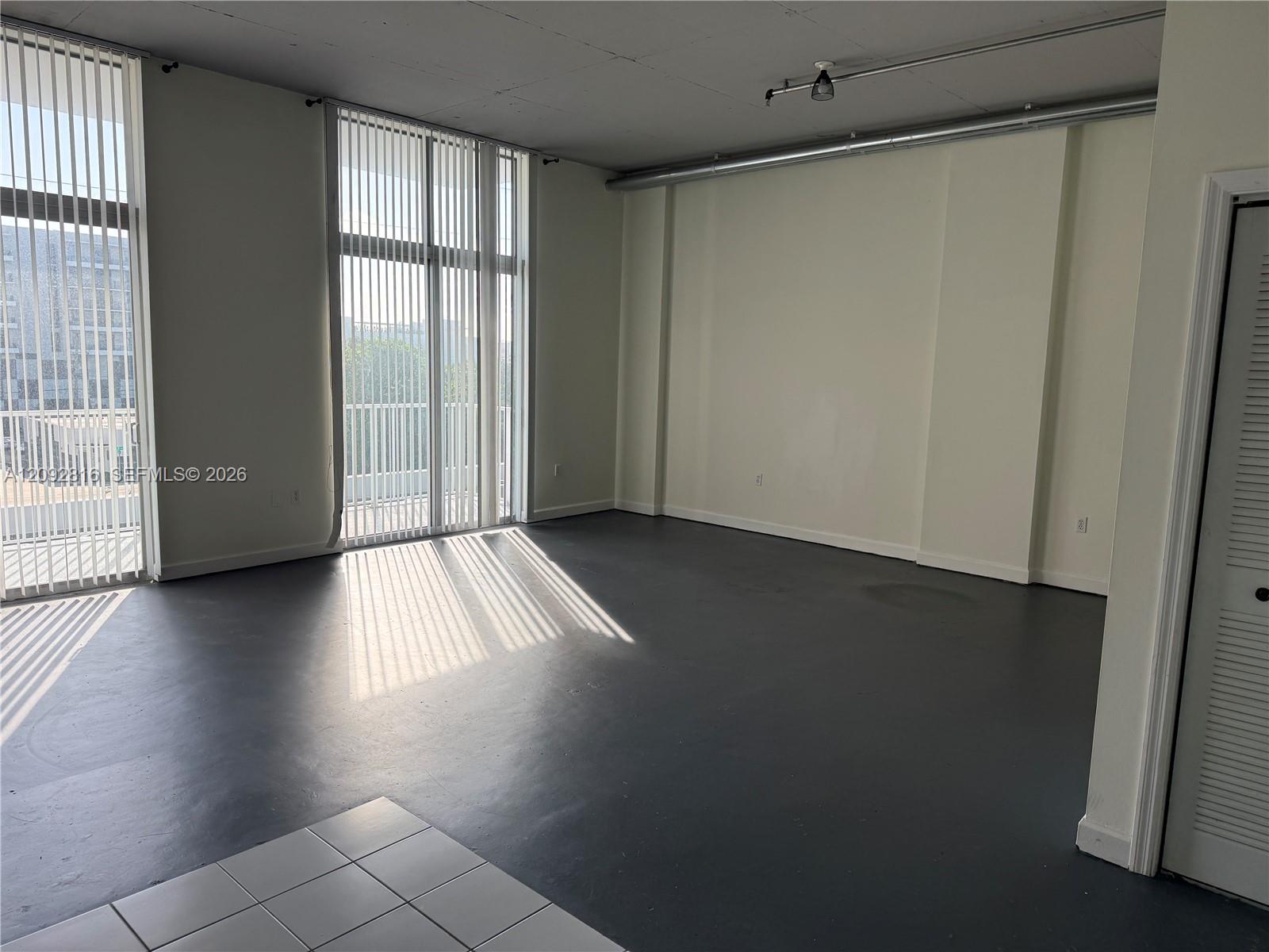 Expansive room with dark flooring, multiple floor-to-ceiling windows, and vertical blinds