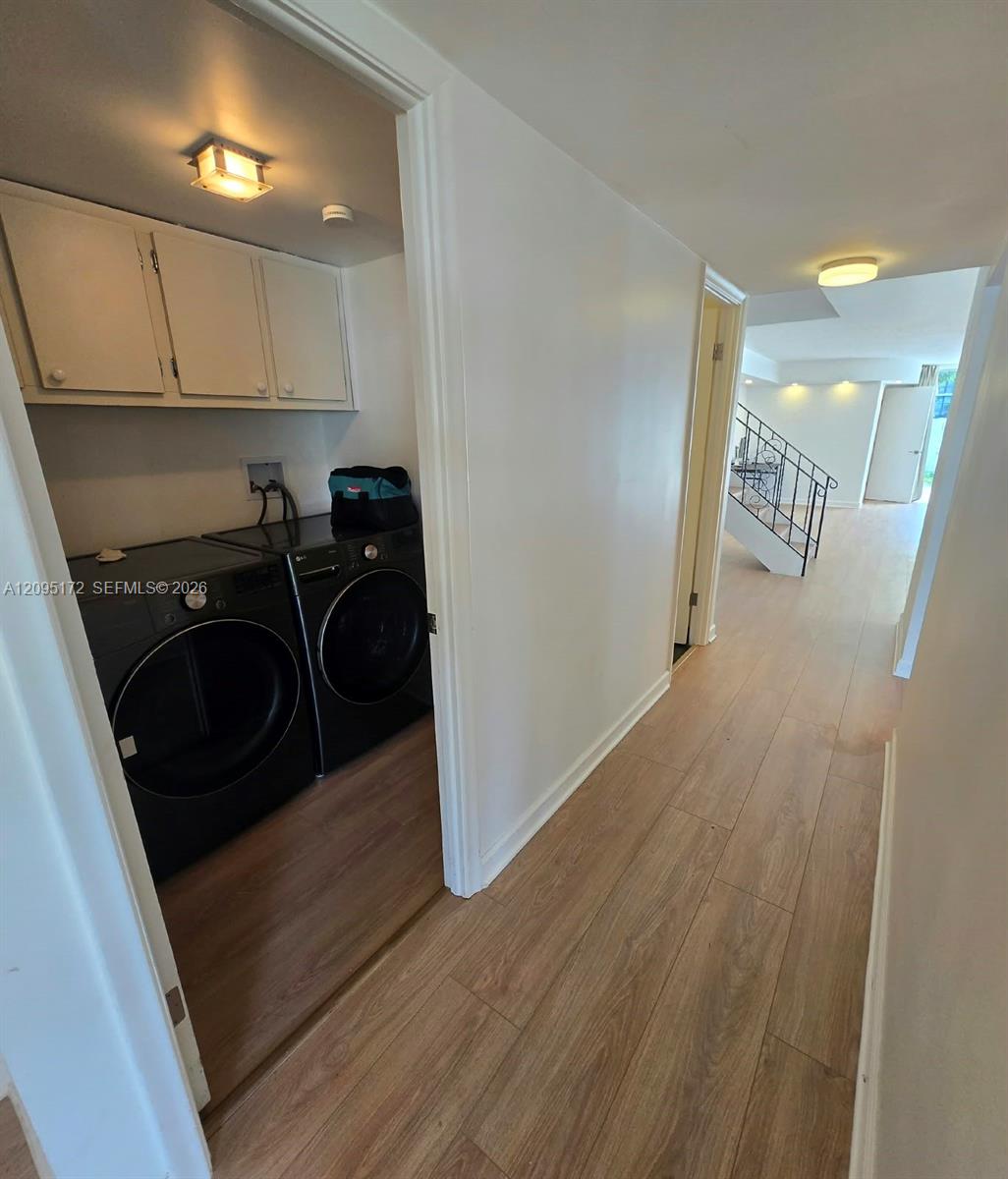 Laundry area featuring white cabinetry and wood-finish flooring, complemented by an open hallway with a staircase