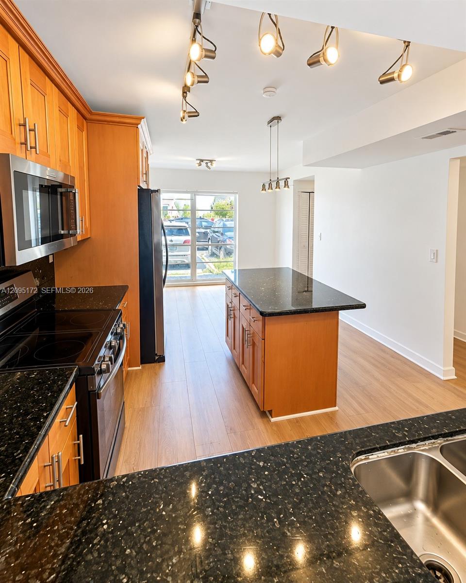 Kitchen featuring natural wood-finish cabinetry, dark stone countertops, stainless steel appliances, a central kitchen island, and multi-directional track lighting