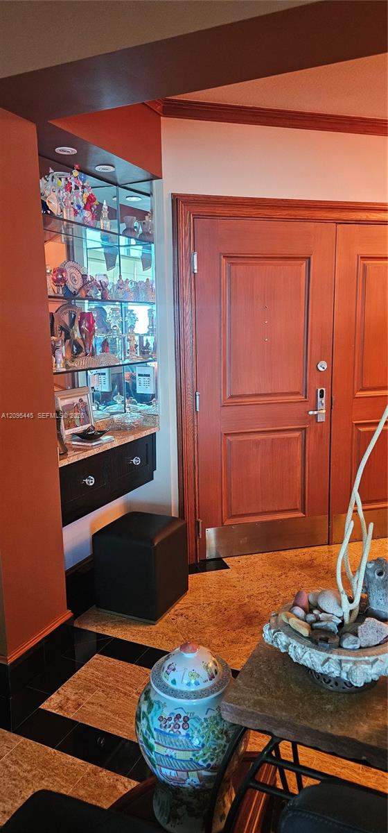 Built-in recessed display niche featuring glass shelving and integrated lighting, double entry doors with natural wood finish, and stone-tiled flooring with decorative inlay