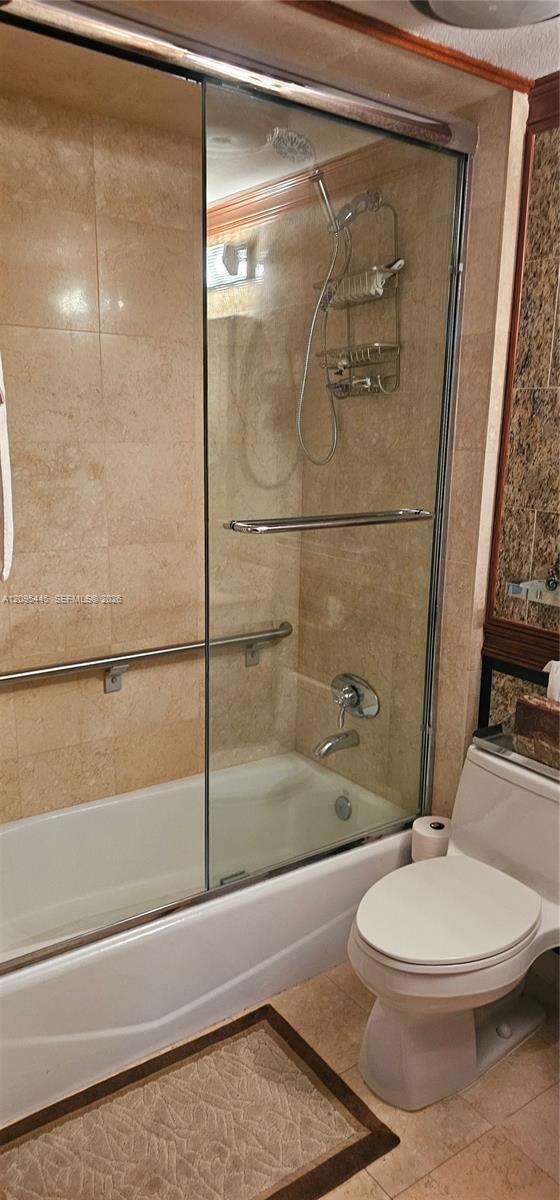 Shower and bathtub combination featuring tile surround, glass sliding enclosure, polished metal hand-held shower fixture, and installed safety bar