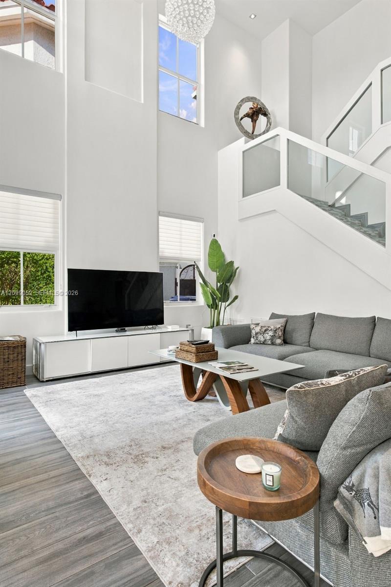 High-ceiling interior featuring multiple oversized windows, wood-finish flooring, glass-panel stair railing, and a tiered spherical chandelier
