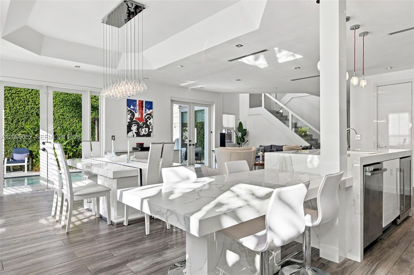 Open-concept interior featuring a coffered ceiling, stone-surfaced waterfall island, wood-finish flooring, glass pendant lighting, and multi-panel glass doors