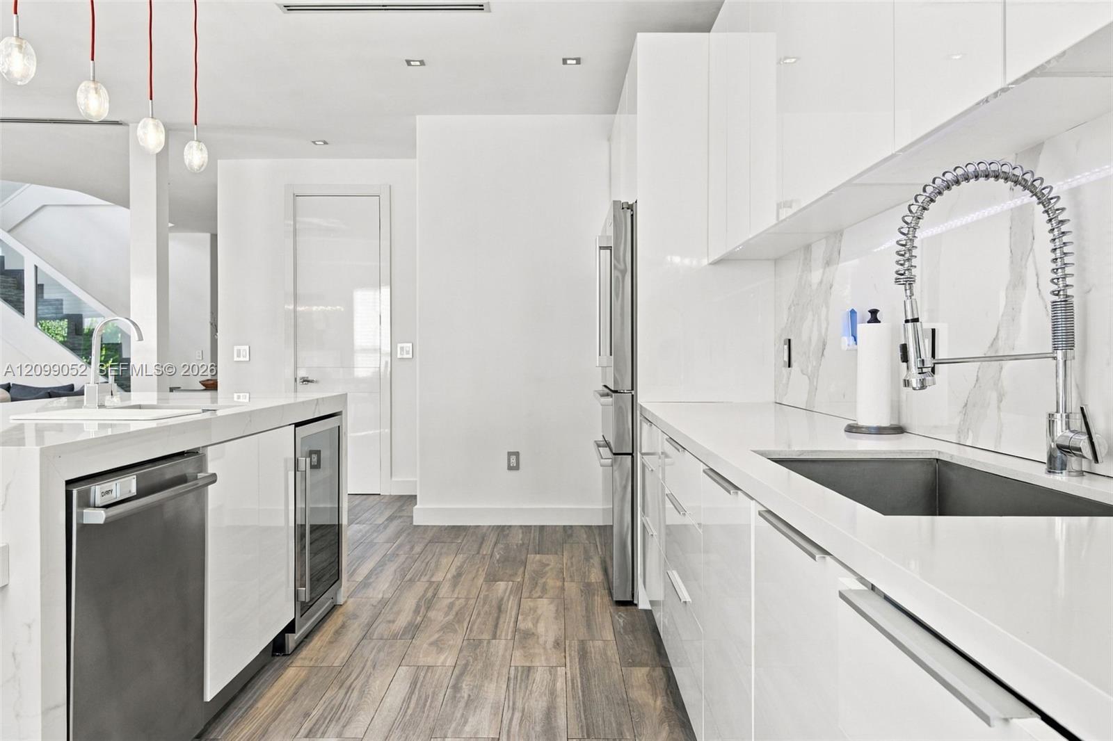 Kitchen featuring high-gloss white cabinetry, white stone countertops, integrated stainless steel appliances, a pull-down commercial-style faucet, and wood-finish flooring