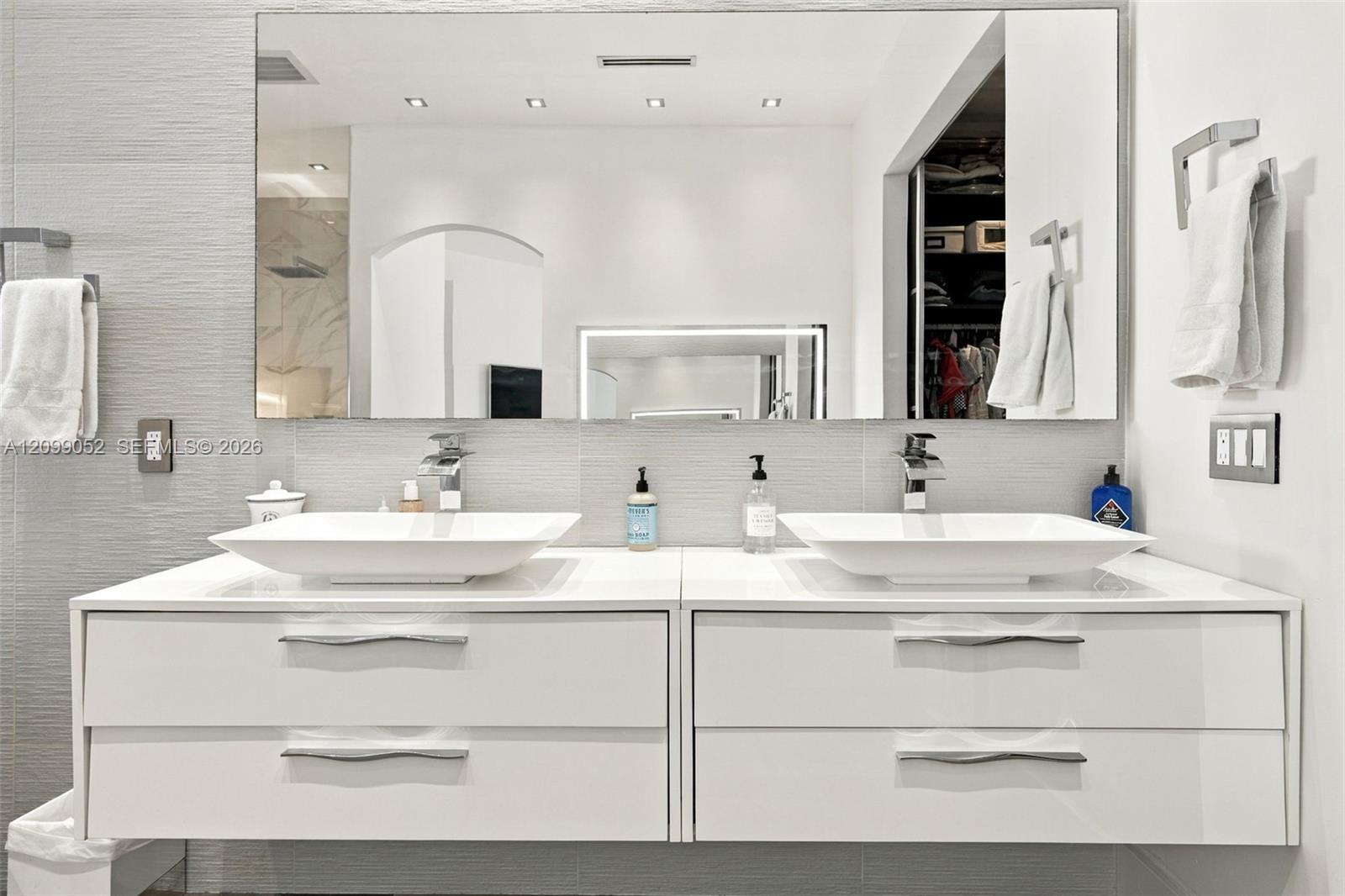 Floating dual vanity featuring white cabinetry, rectangular vessel sinks, chrome faucets, and large wall-mounted mirror with recessed lighting