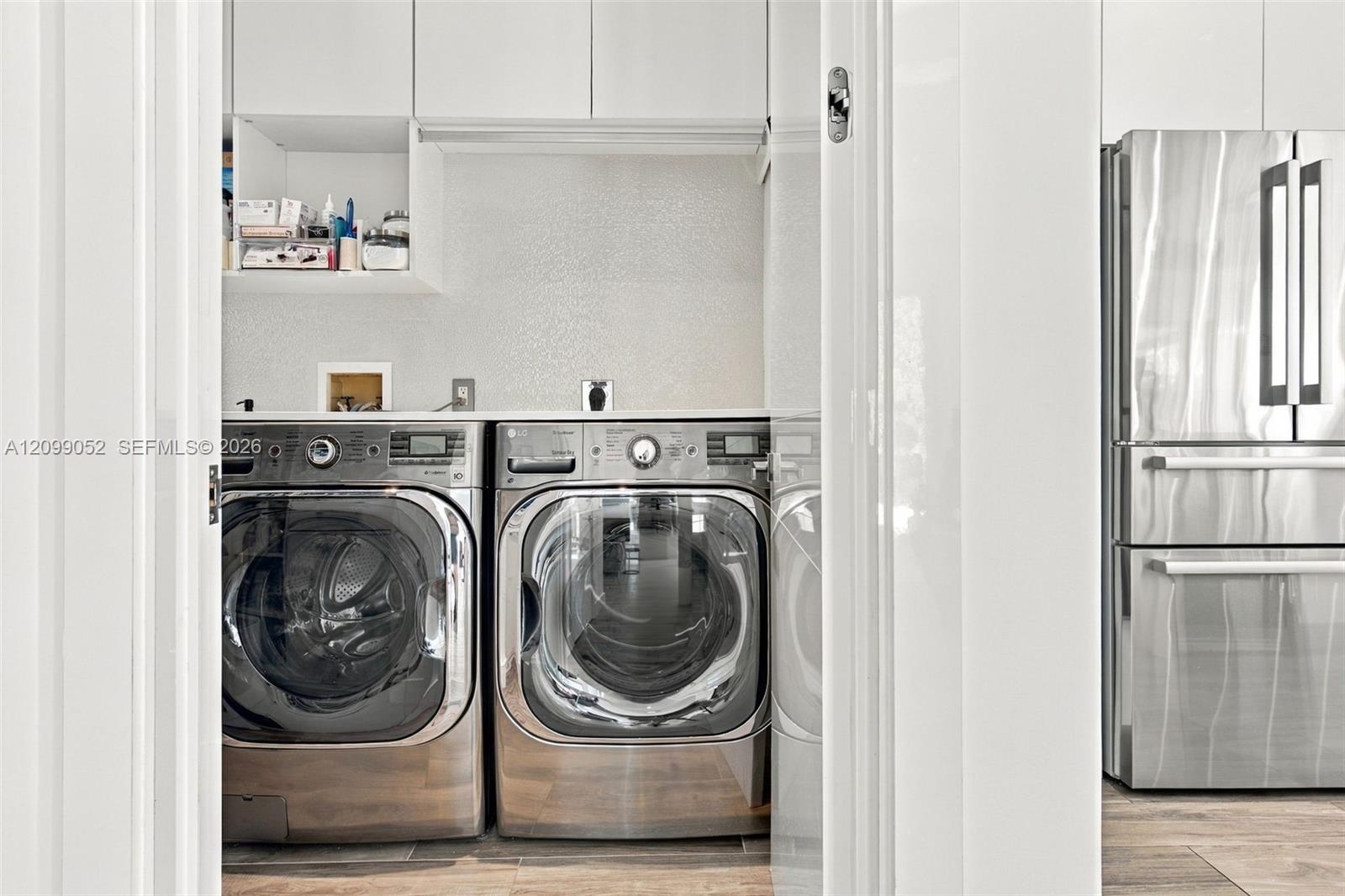Laundry area featuring white cabinetry, custom shelving, a solid-surface countertop, and stainless steel appliances
