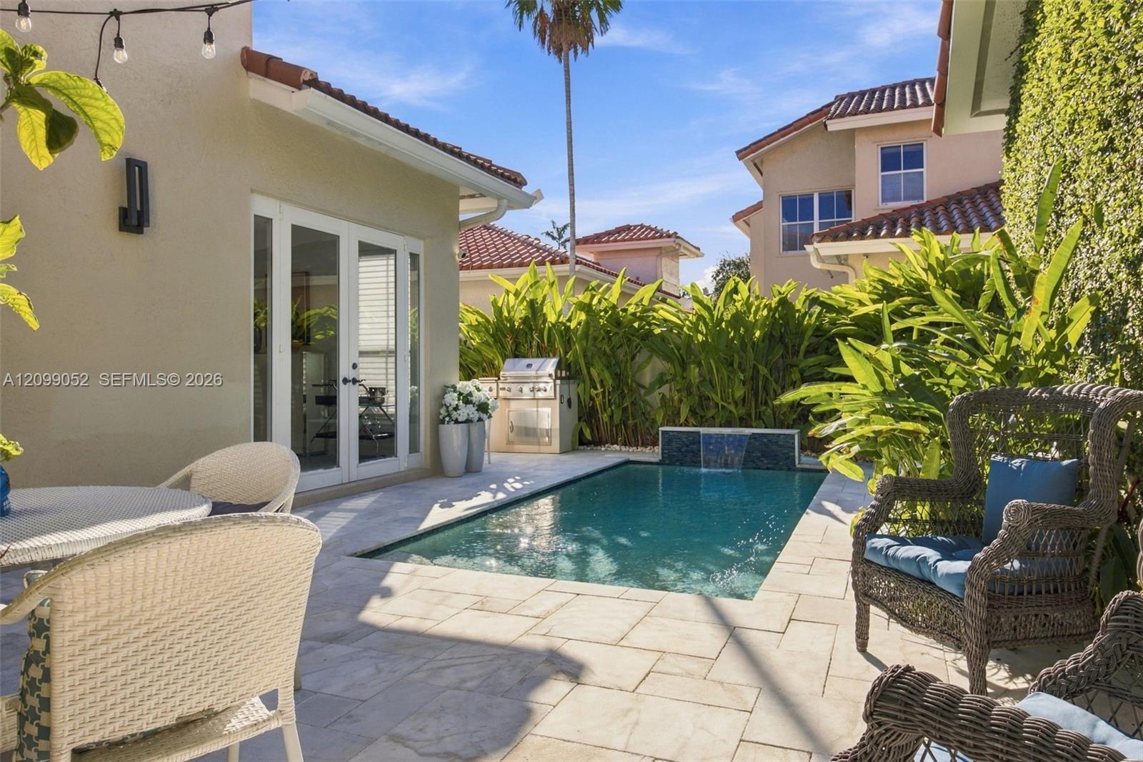 Outdoor living space featuring a tiled patio, private swimming pool with a stone-accented water feature, built-in stainless steel grill, and manicured perimeter landscaping