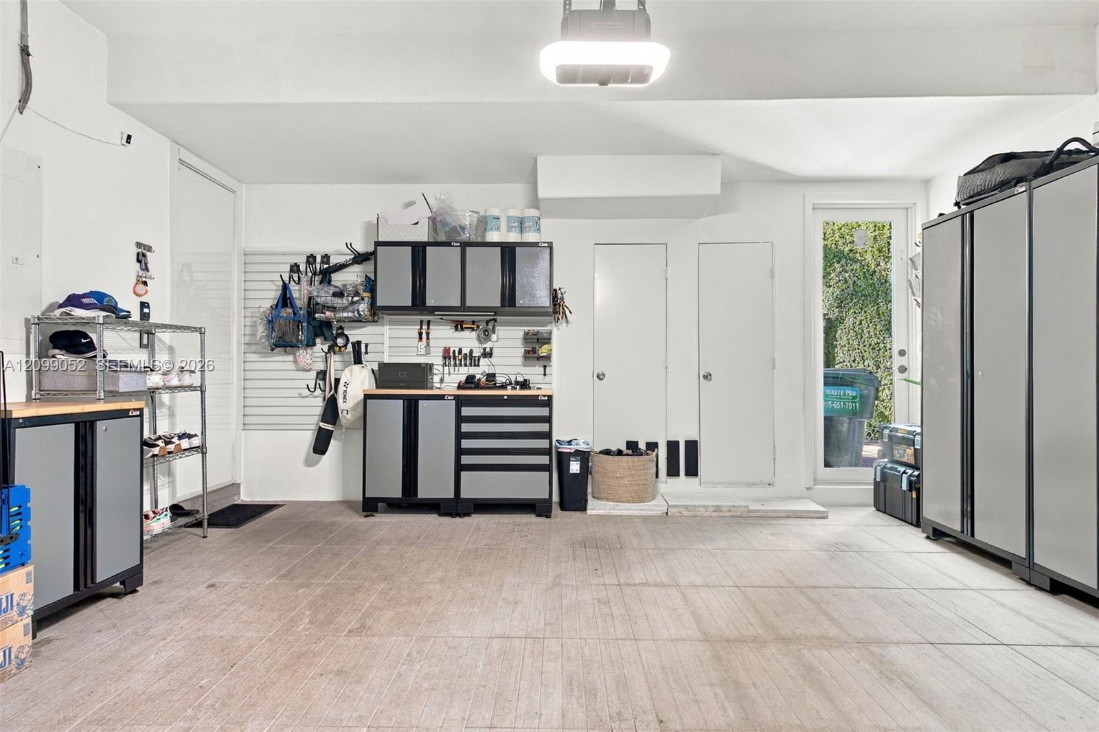 Finished garage featuring integrated wall-mounted storage panels, custom built-in cabinetry with metal-finish doors, durable concrete flooring, and a glass-paneled exterior door