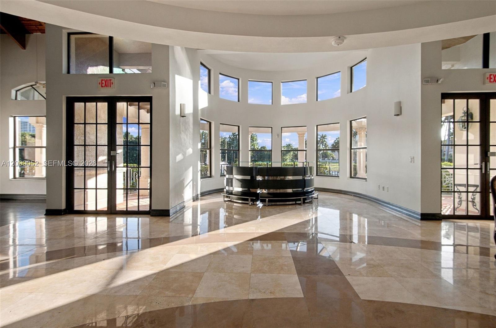 Rotunda interior featuring polished stone flooring, a multi-paneled curved window wall, and dual glass-paned double doors