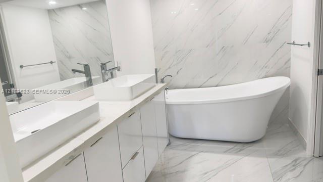 Freestanding soaking tub featuring a chrome floor-mounted faucet with a handheld sprayer, set against wall and floor tile with a veined pattern