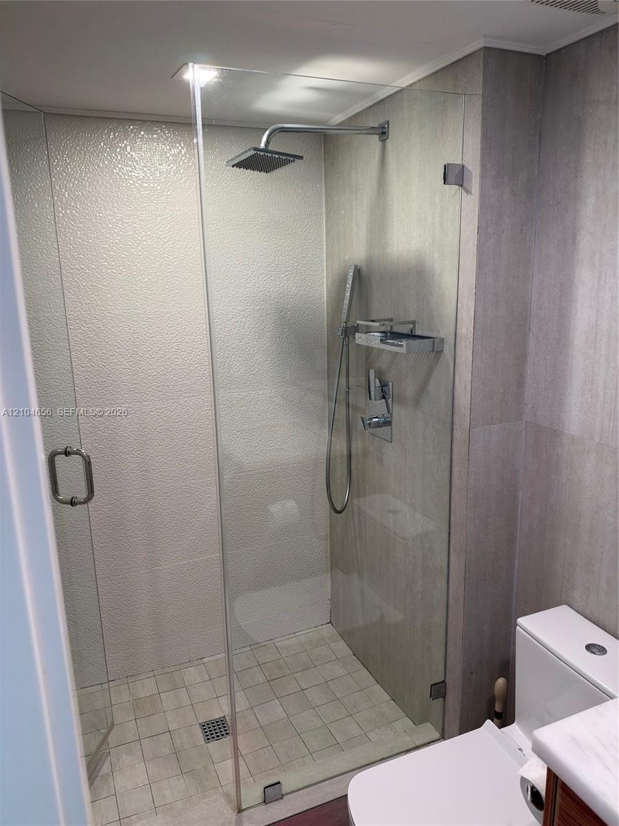 Walk-in shower featuring a frameless glass enclosure, rainfall showerhead, integrated handheld sprayer, and stone-finish tile surround