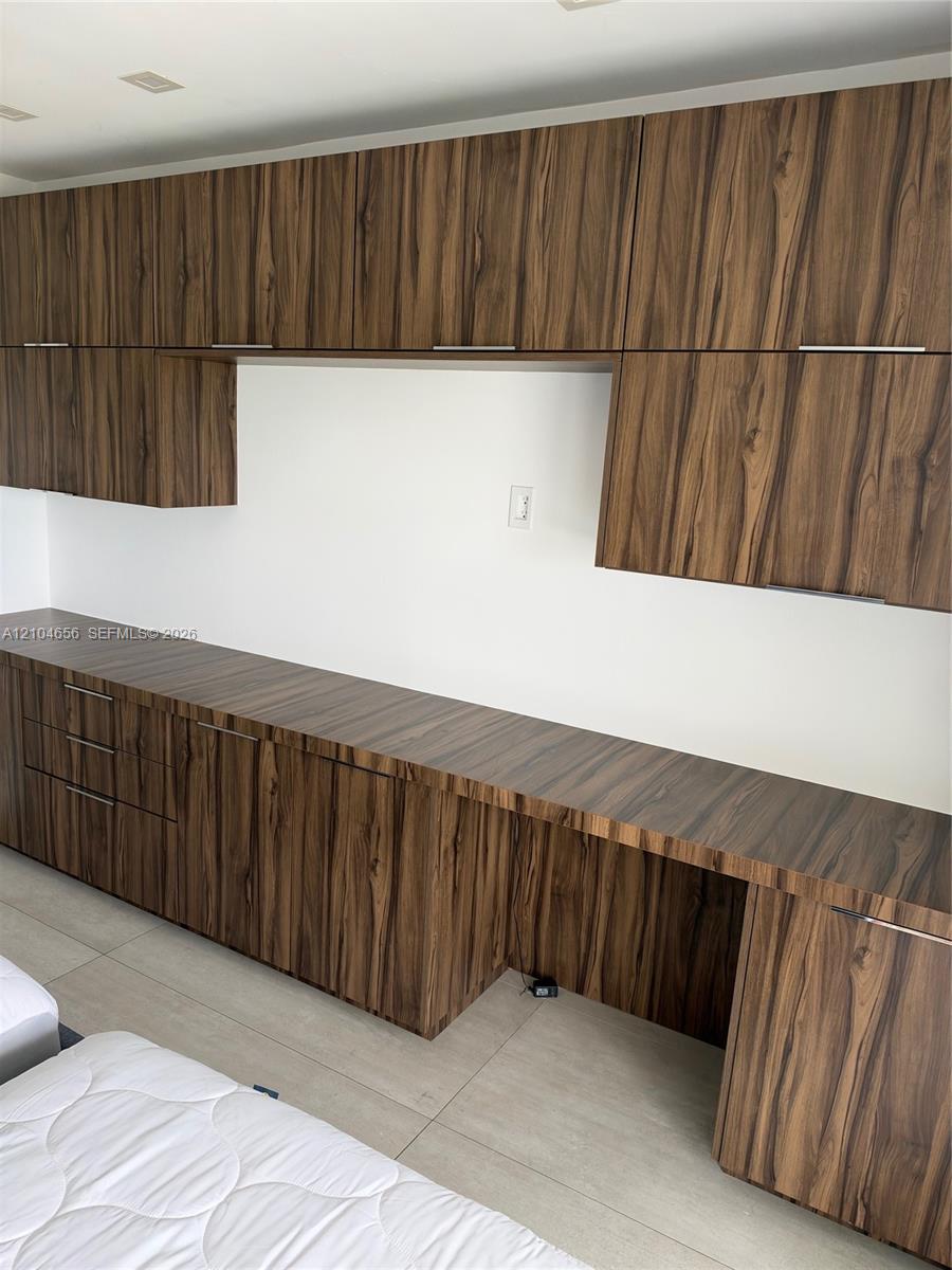 Custom built-in cabinetry featuring wood-finish cabinetry, sleek horizontal pulls, extensive countertop surface, and recessed ceiling lighting