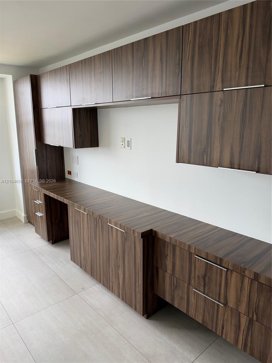 Built-in cabinetry with wood-finish flat-panel doors, integrated desk surface, matte-finish hardware, and tile flooring