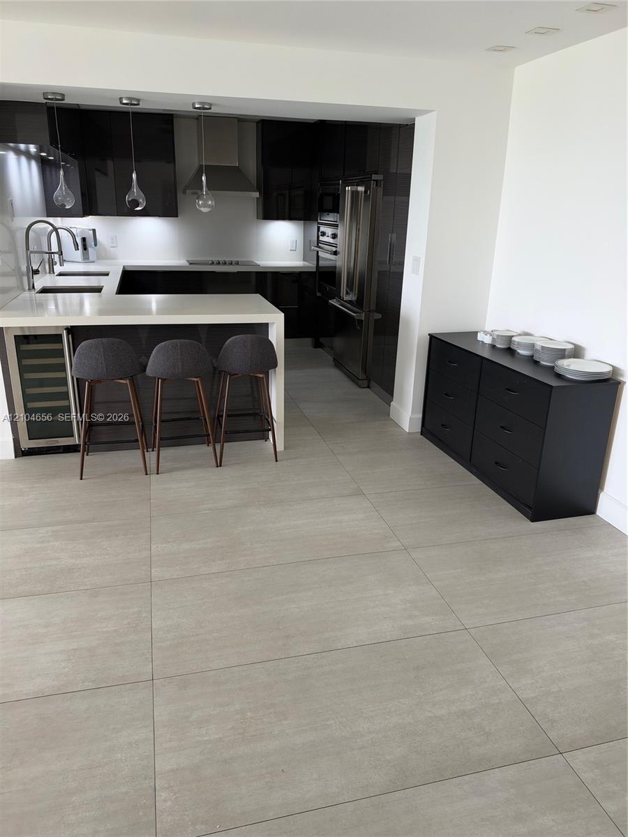 Kitchen featuring flat-panel cabinetry, light-toned stone-finish countertops, stainless steel appliances, a built-in wine cooler, and large-format porcelain tile flooring