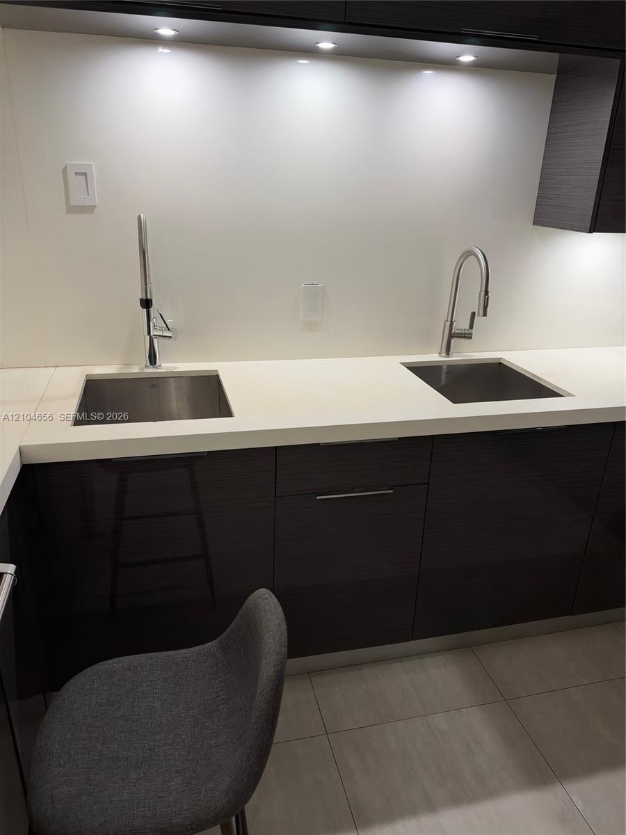 Dual stainless steel under-mount sinks with high-arc gooseneck faucets, smooth white countertops, and dark, high-gloss cabinetry with recessed lighting
