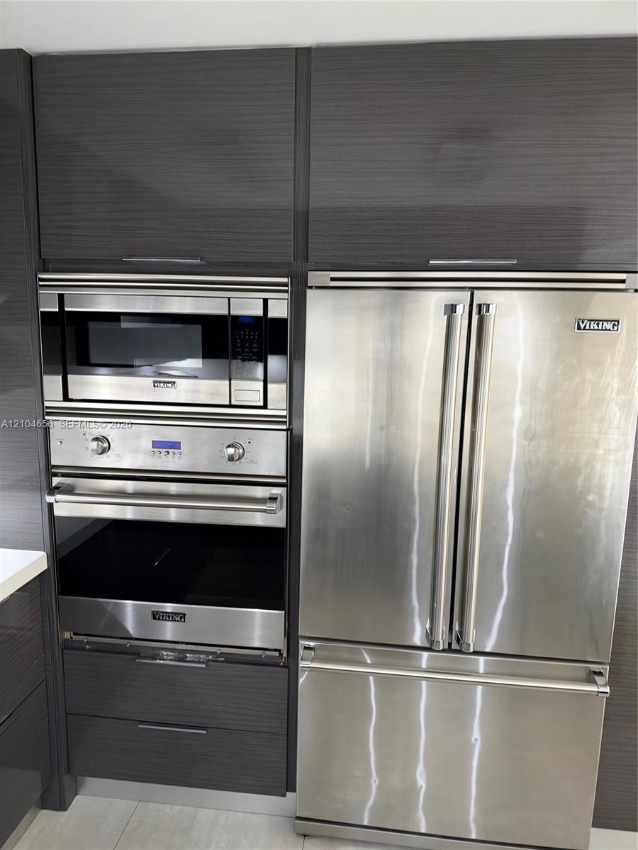 High-gloss, dark-toned cabinetry featuring integrated stainless steel Viking appliances, including a French-door refrigerator, a built-in microwave, and a wall oven