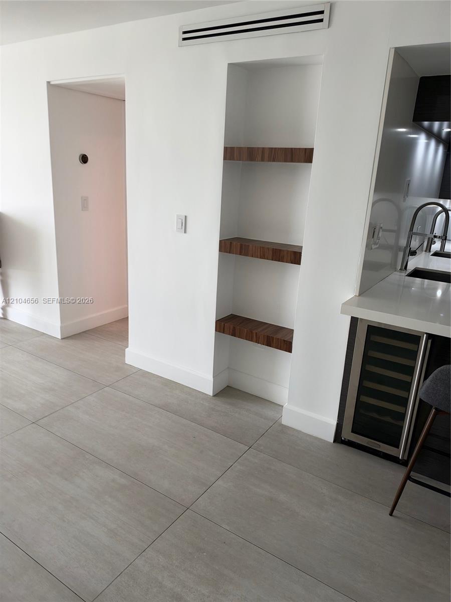 Built-in recessed shelving with wood-finish floating tiers, large-format tile flooring, and integrated under-counter beverage refrigerator with a solid surface countertop