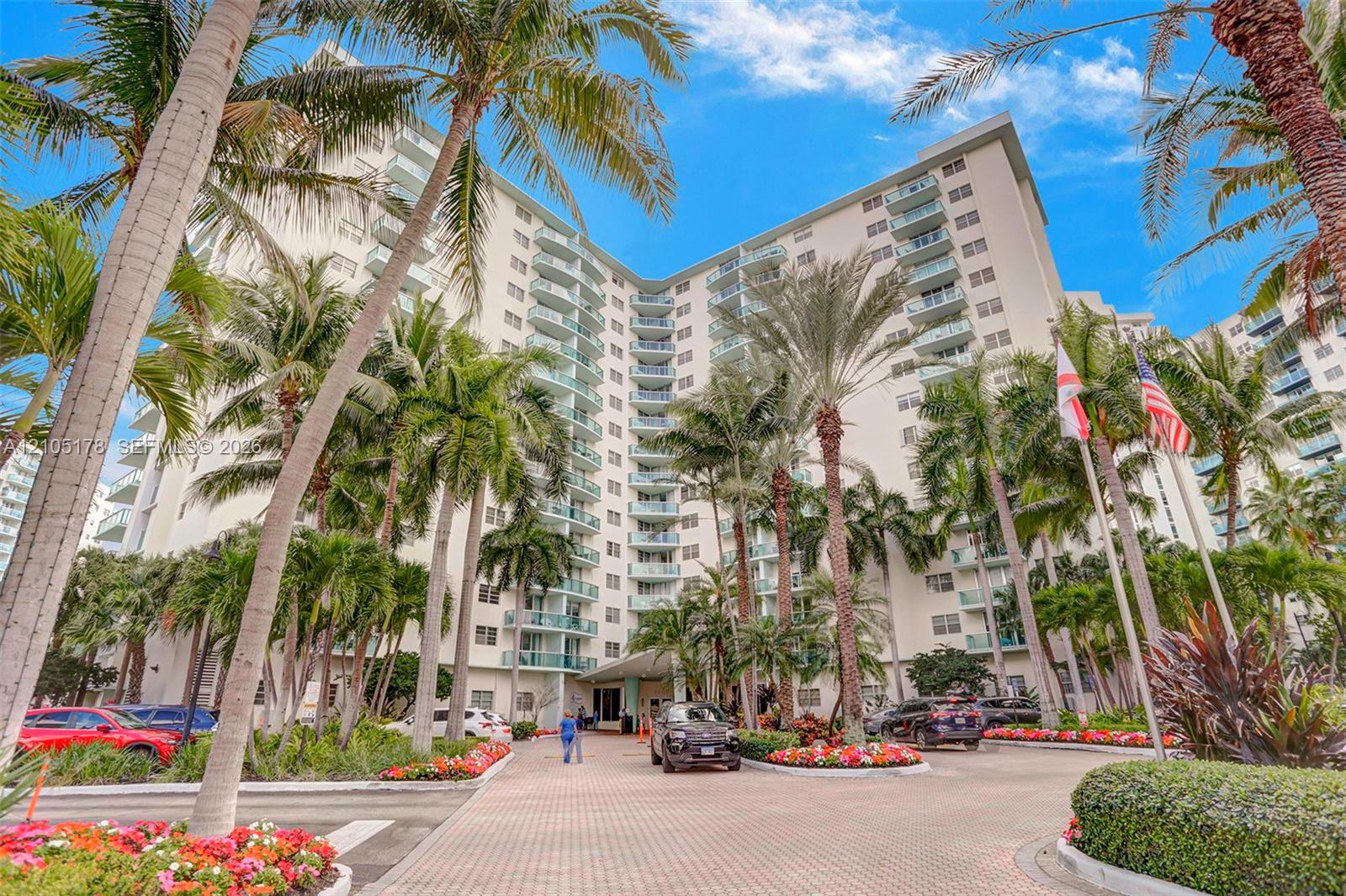 High-rise building exterior featuring tiered private balconies, paved motor court, and lush tropical landscaping with mature palm trees