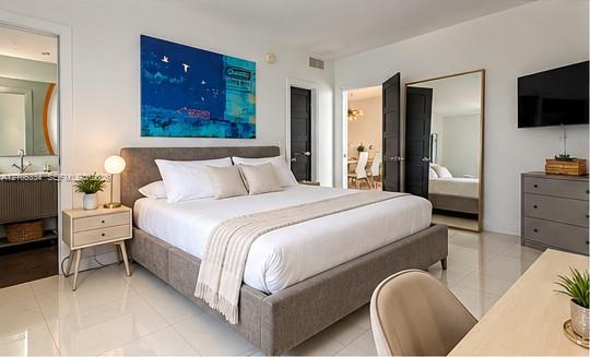 White tile flooring throughout, large full-length mirror, dark paneled doors, and an adjoining space with a vanity