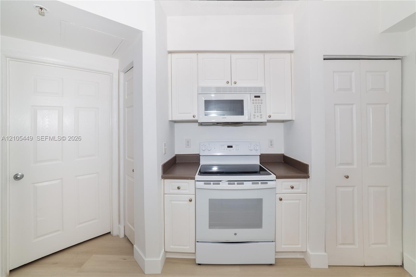 Kitchen featuring white cabinetry, white range, built-in microwave, and wood-finish flooring