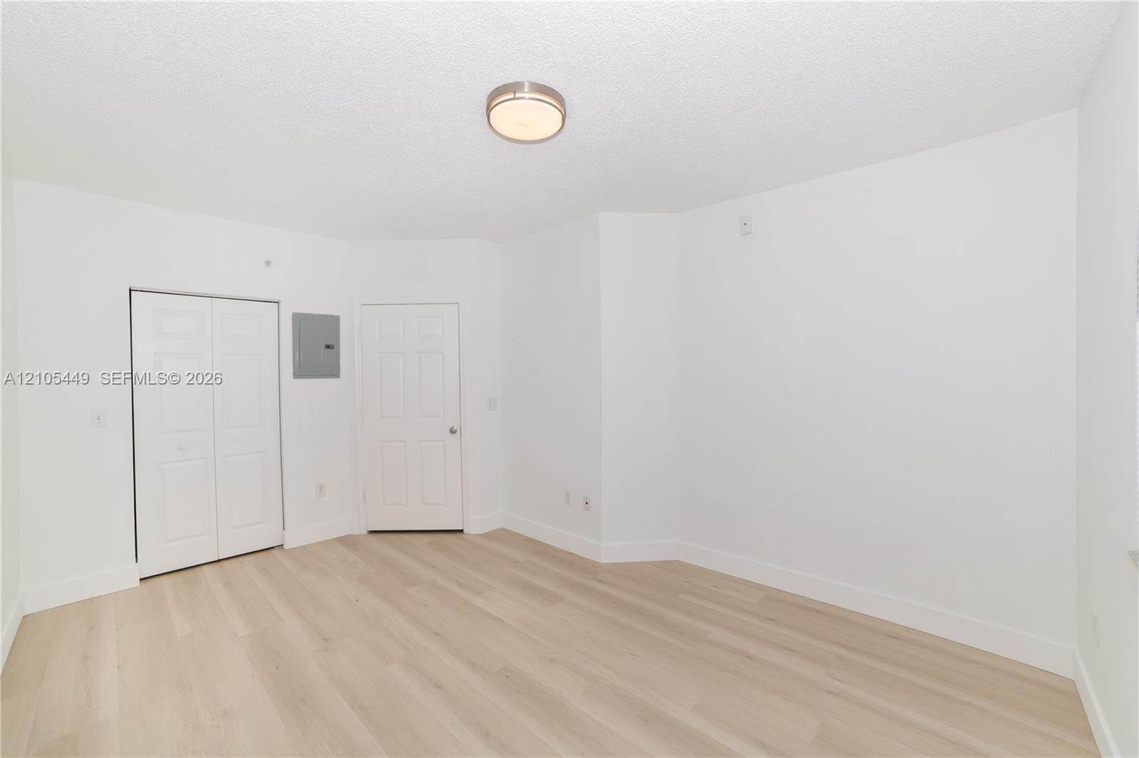 Light-toned wood-finish flooring, white walls, flush-mount ceiling fixture, and bi-fold closet doors