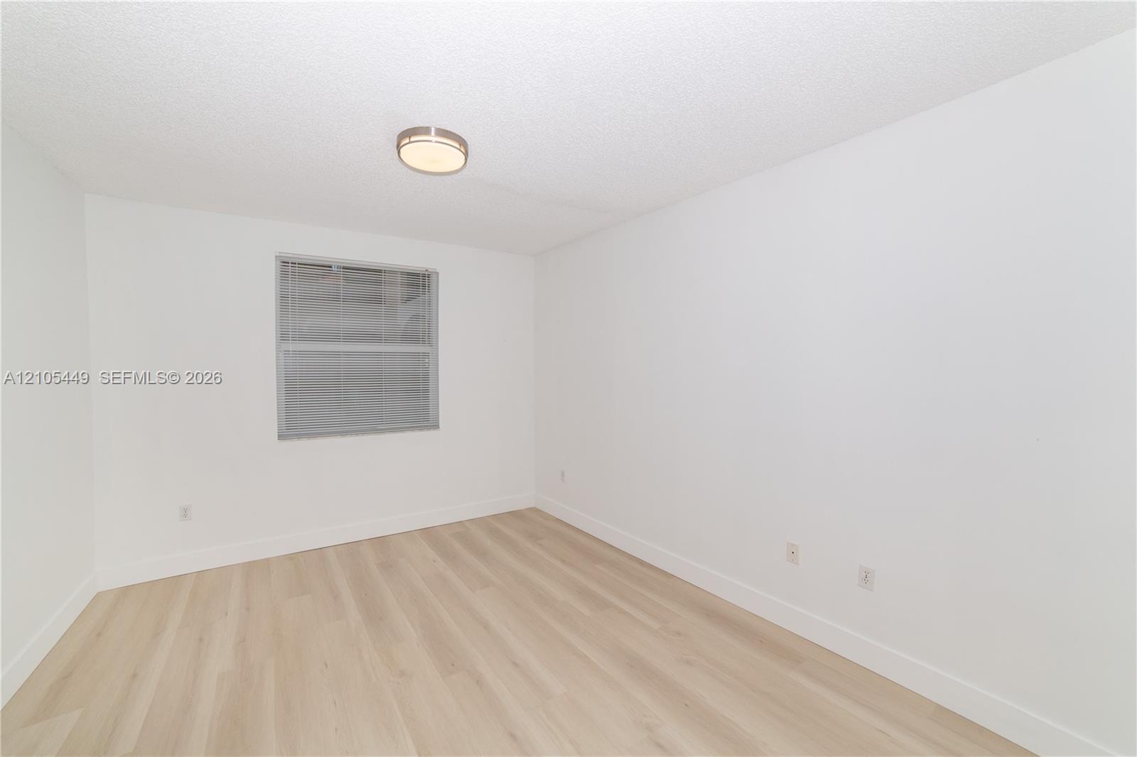 Neutral white walls, wood-finish flooring, and a flush mount ceiling light fixture