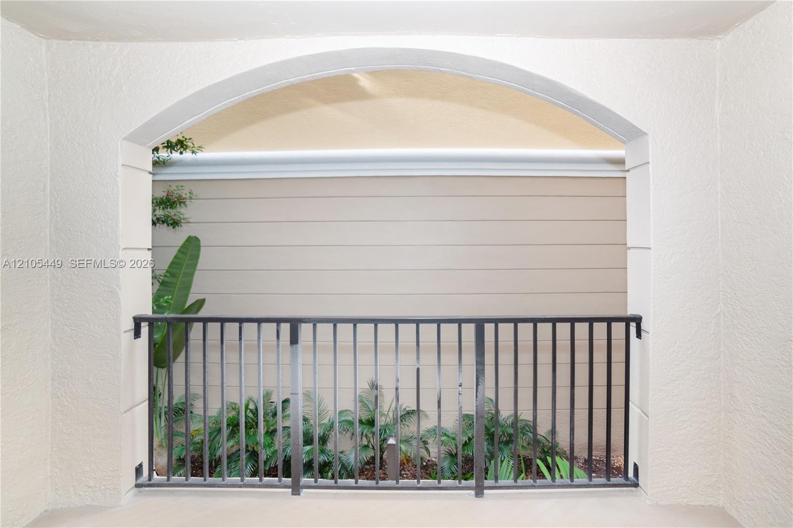 Archway entry to an outdoor space with black metal railing, stucco walls, and integrated landscaping
