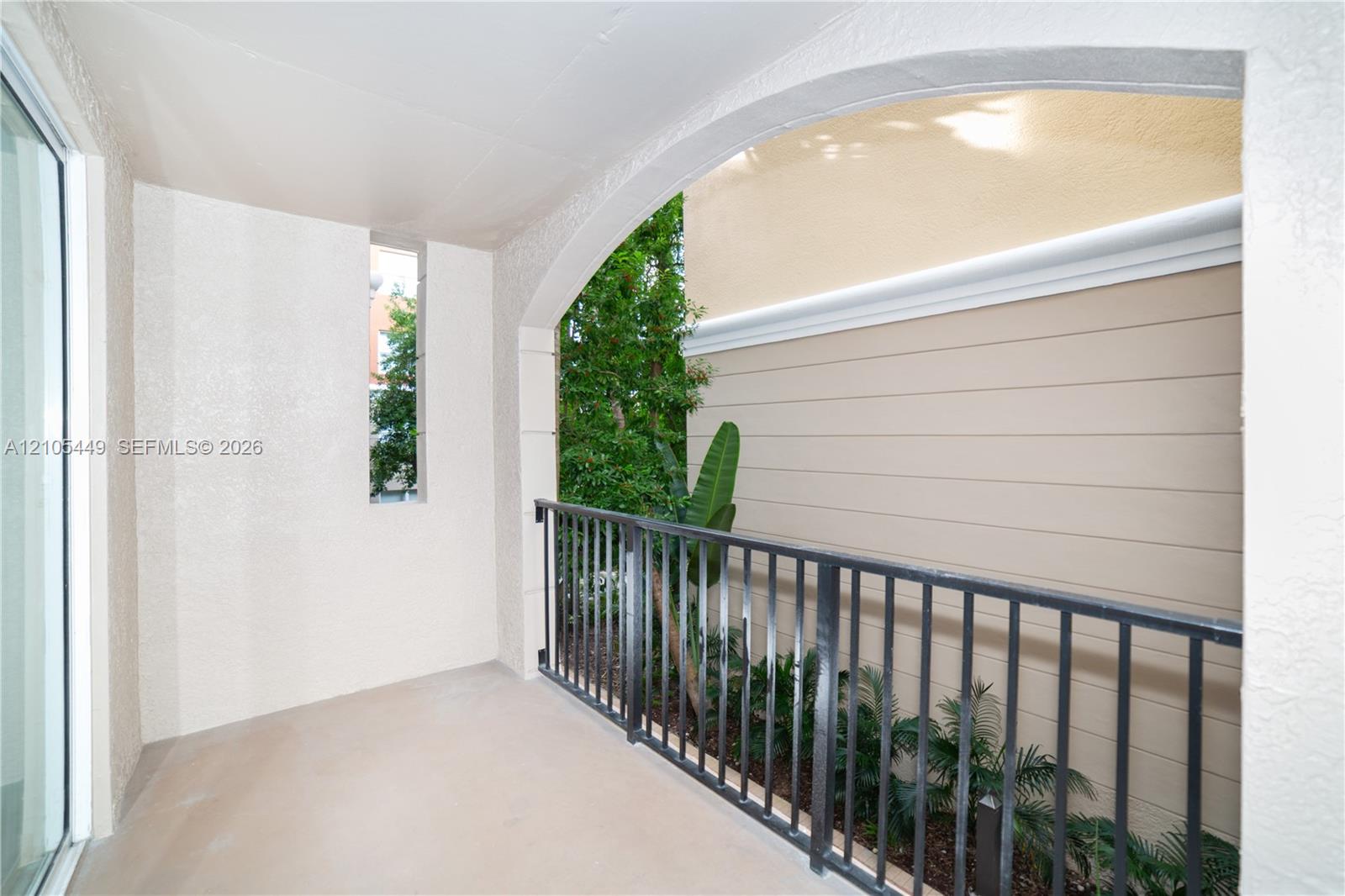 Private outdoor balcony with stucco walls, an arched entrance, and a dark-toned metal railing