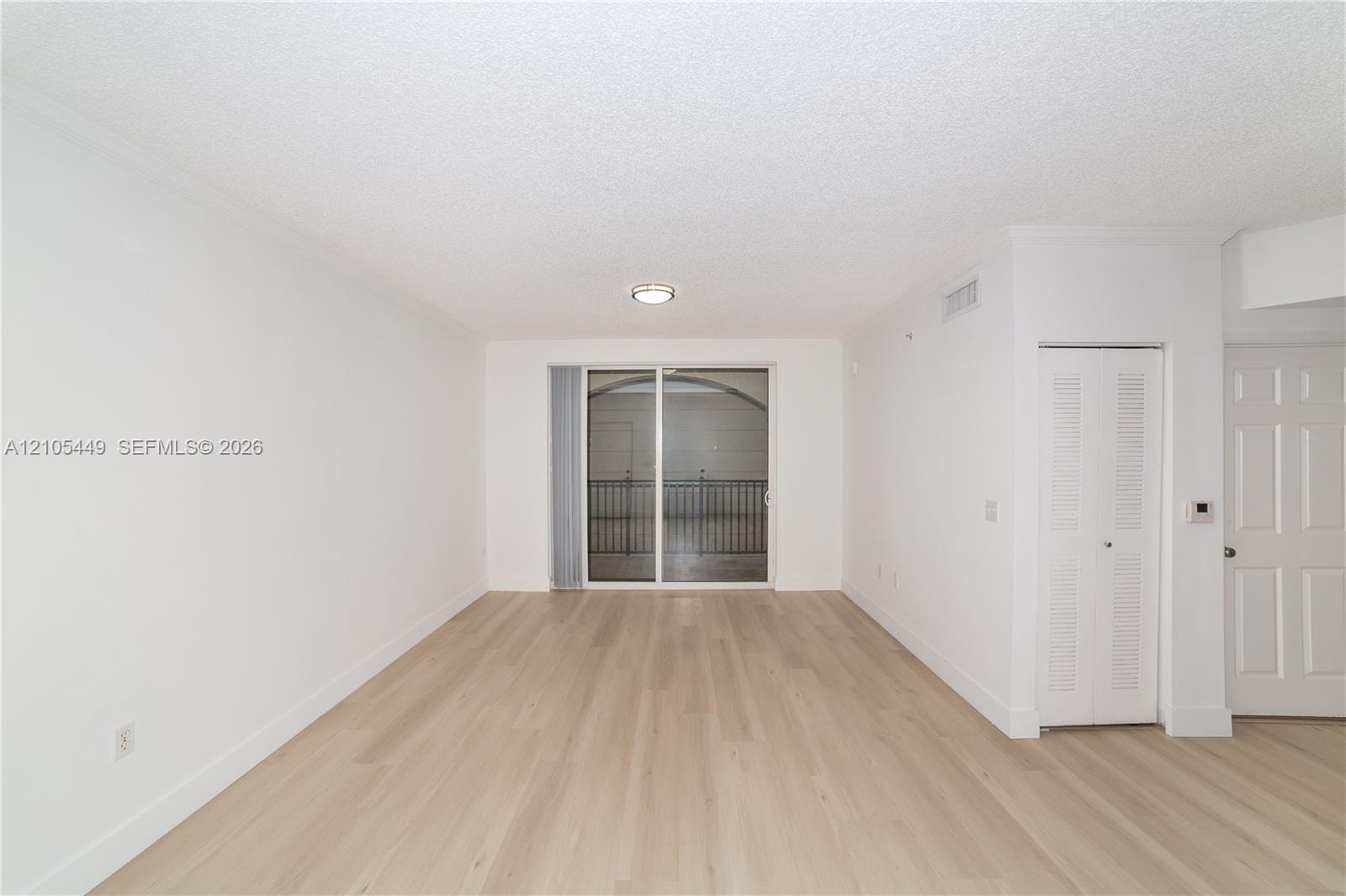 Spacious room featuring wood-finish flooring, crown molding, and a sliding glass door to a private balcony