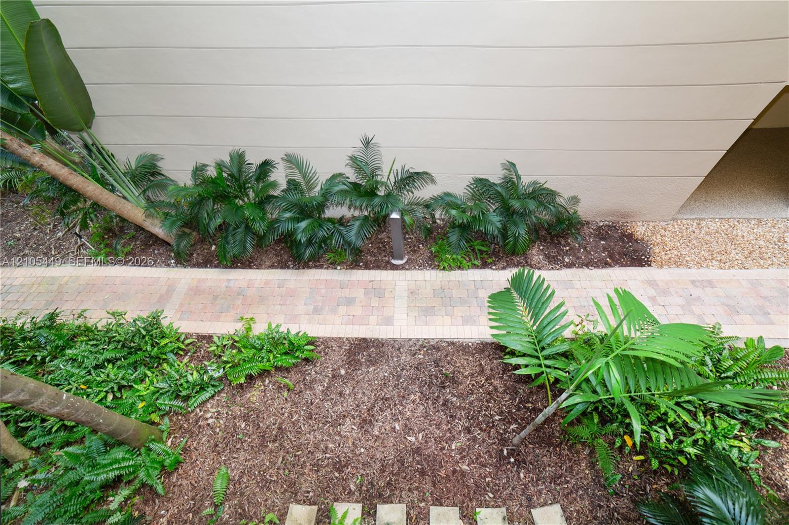 Paver walkway bordered by lush tropical plantings and mulched beds