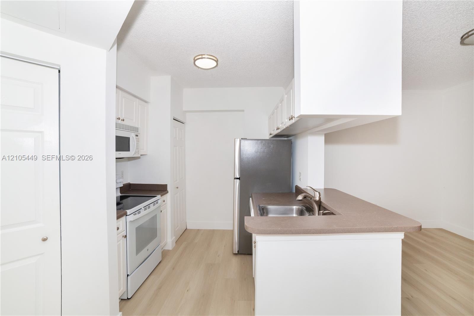 Kitchen featuring white cabinetry, a stainless steel refrigerator, white range, built-in microwave, and wood-finish flooring