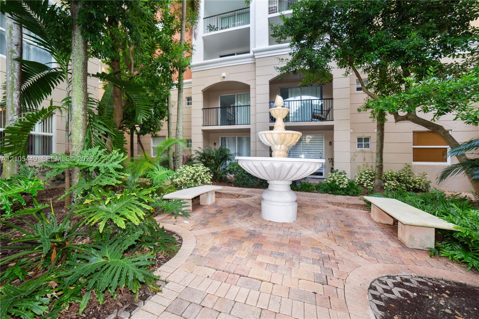 Tiered fountain feature with a surrounding paver pathway and mature tropical landscaping