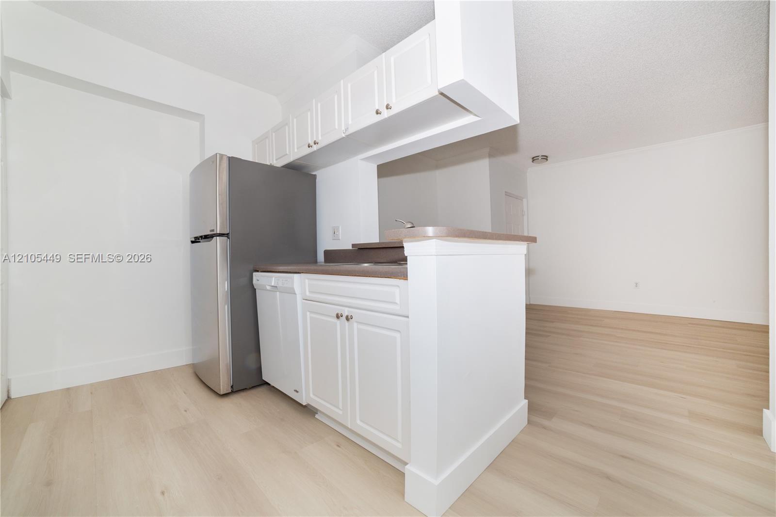 White cabinetry with brushed nickel hardware, stainless steel refrigerator, integrated dishwasher, and wood-finish flooring