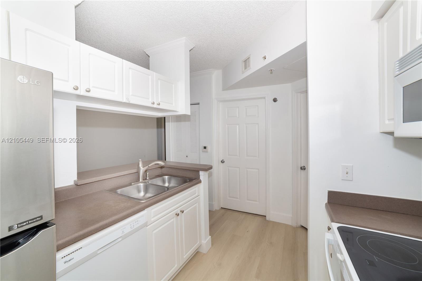 Kitchen featuring white cabinetry, dual stainless steel sink, stainless steel refrigerator, and wood-finish flooring
