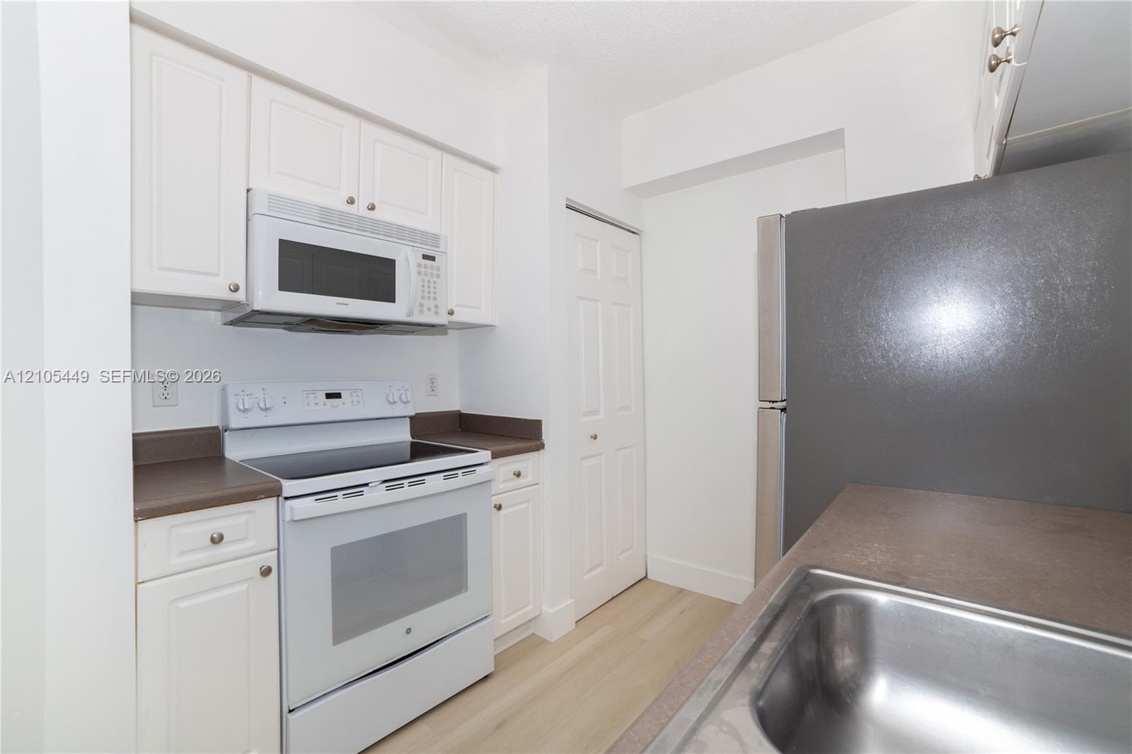 Kitchen featuring white cabinetry, a stainless steel sink, an electric range, an over-the-range microwave, and light wood-finish flooring