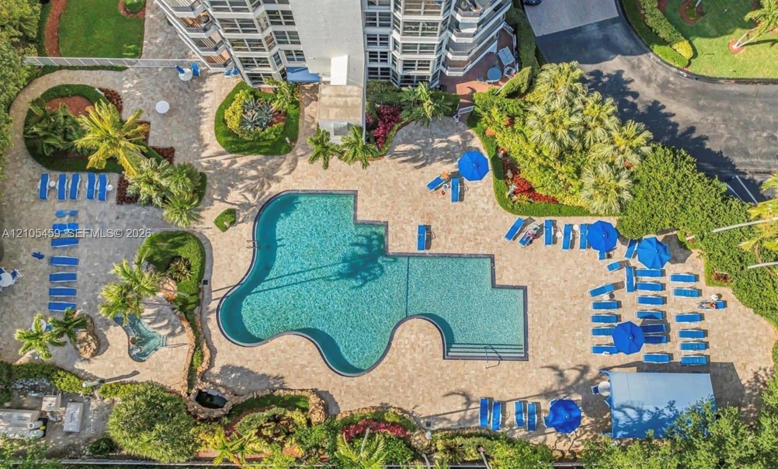 Expansive outdoor amenity area featuring a freeform swimming pool, extensive paver decking, and lush tropical landscaping
