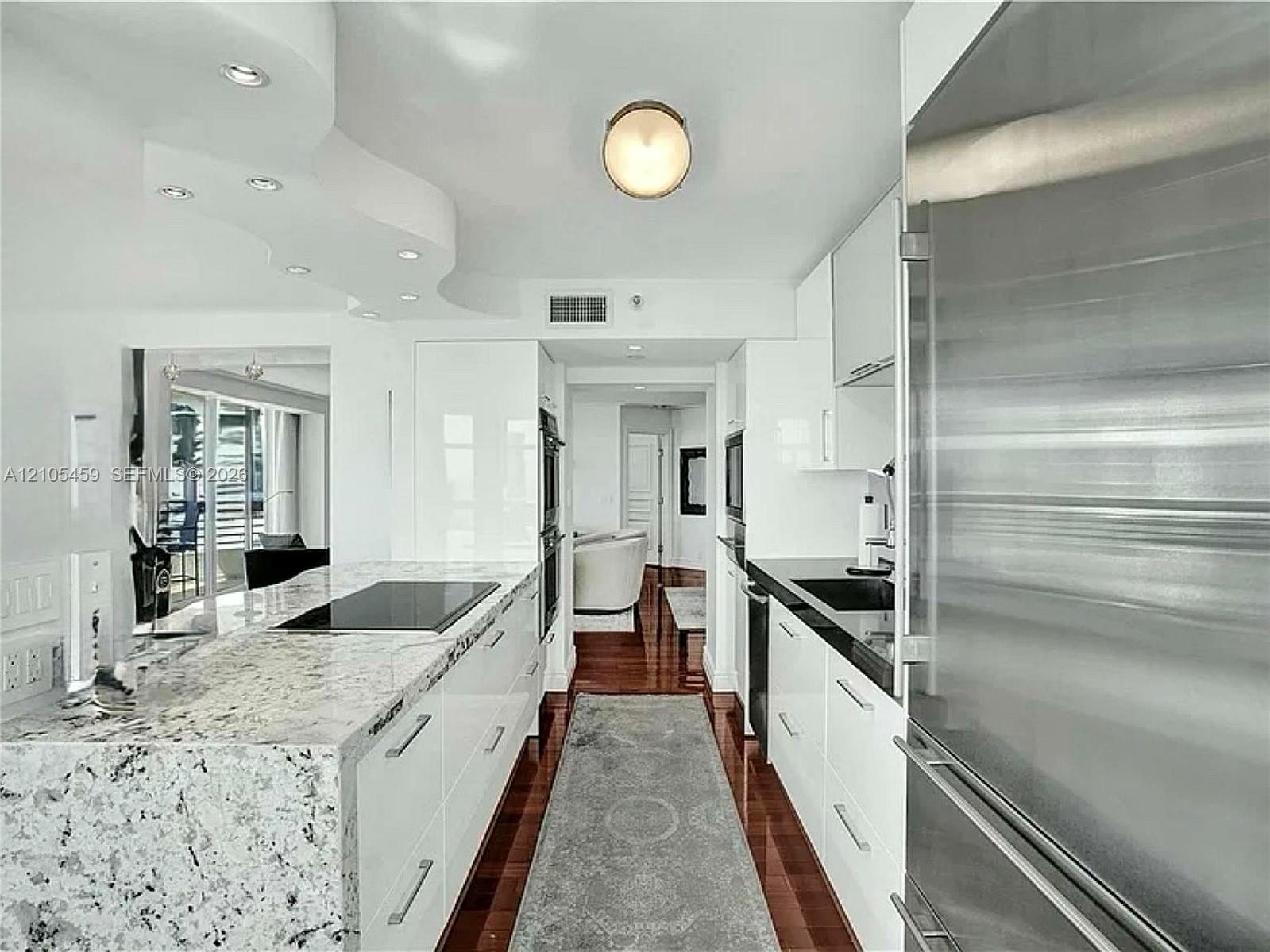 Modern kitchen featuring high-gloss white cabinetry, integrated stainless steel appliances, and wood-finish flooring