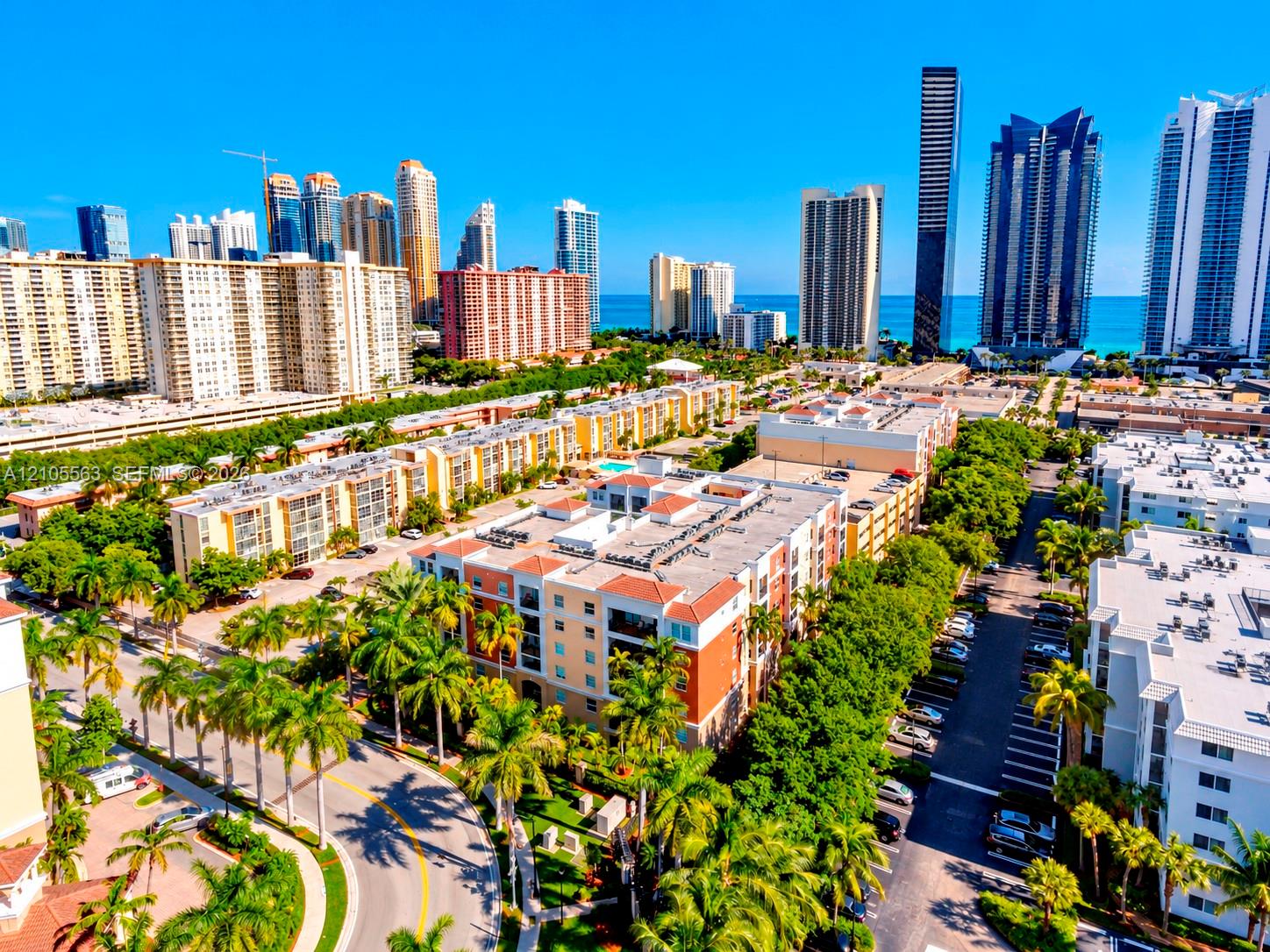 Expansive urban landscape featuring multiple multi-story residential buildings, abundant mature palm trees, and visible clear blue water