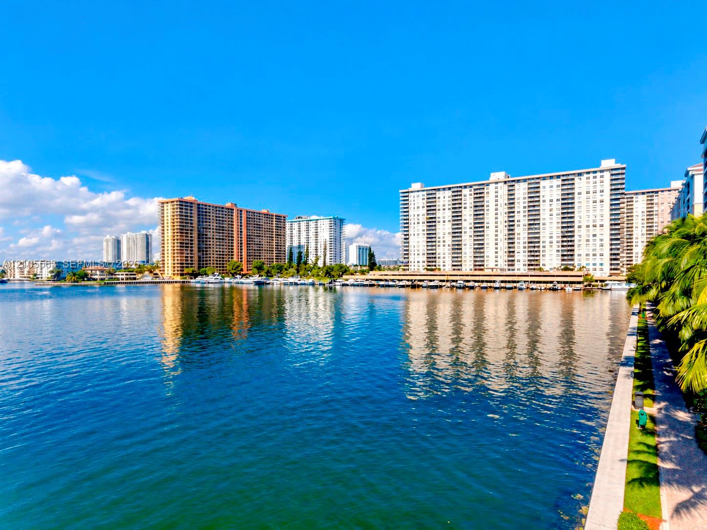 Waterfront high-rise residence showcasing panoramic water vistas, direct waterfront access, multi-building residential complex with varied architectural styles, lush tropical landscaping along the promenade, and sparkling blue-water setting with natural light throughout