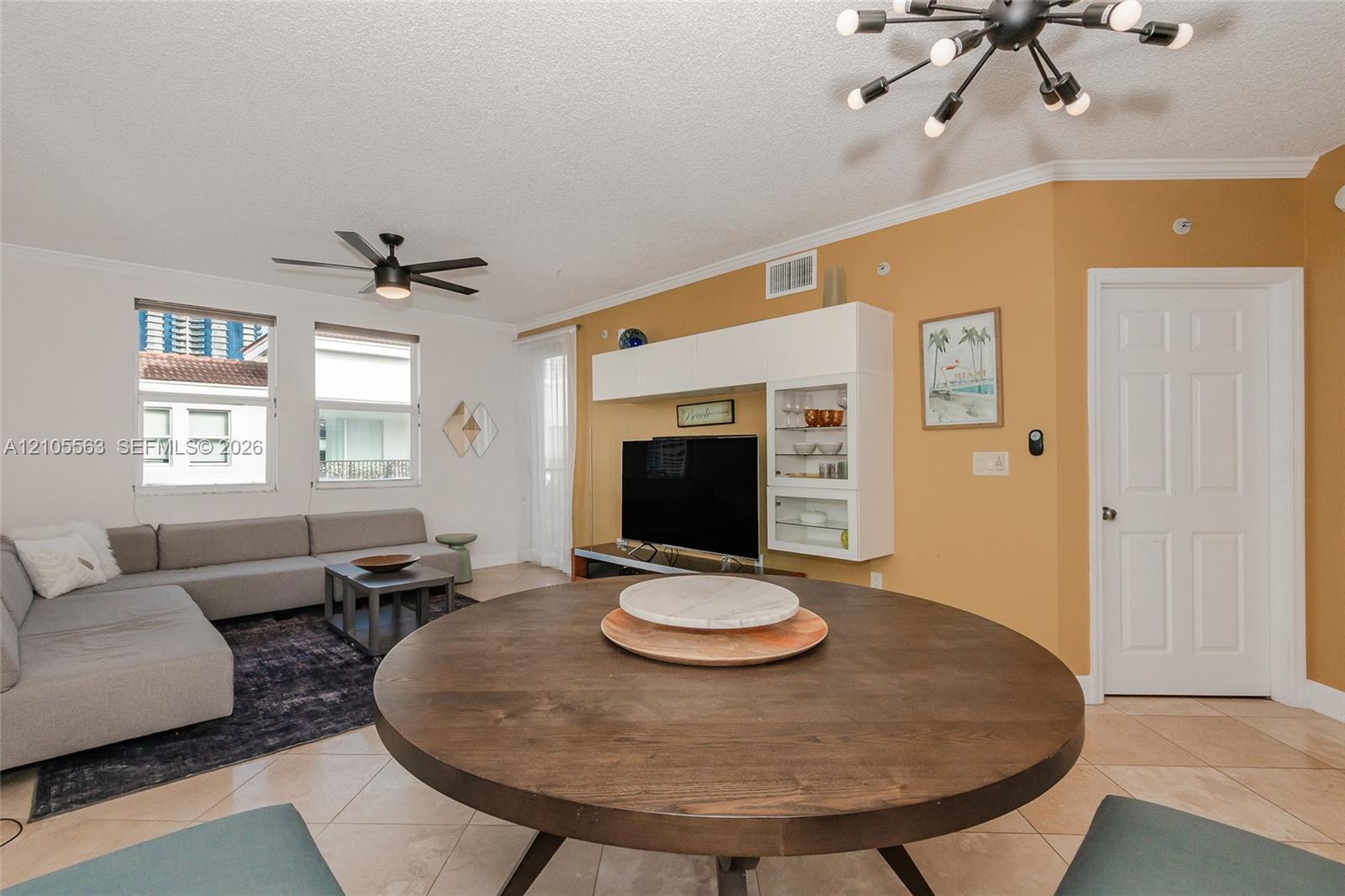 Open-concept living space featuring tile flooring, a dark wood-finish dining table, and a modern ceiling fan