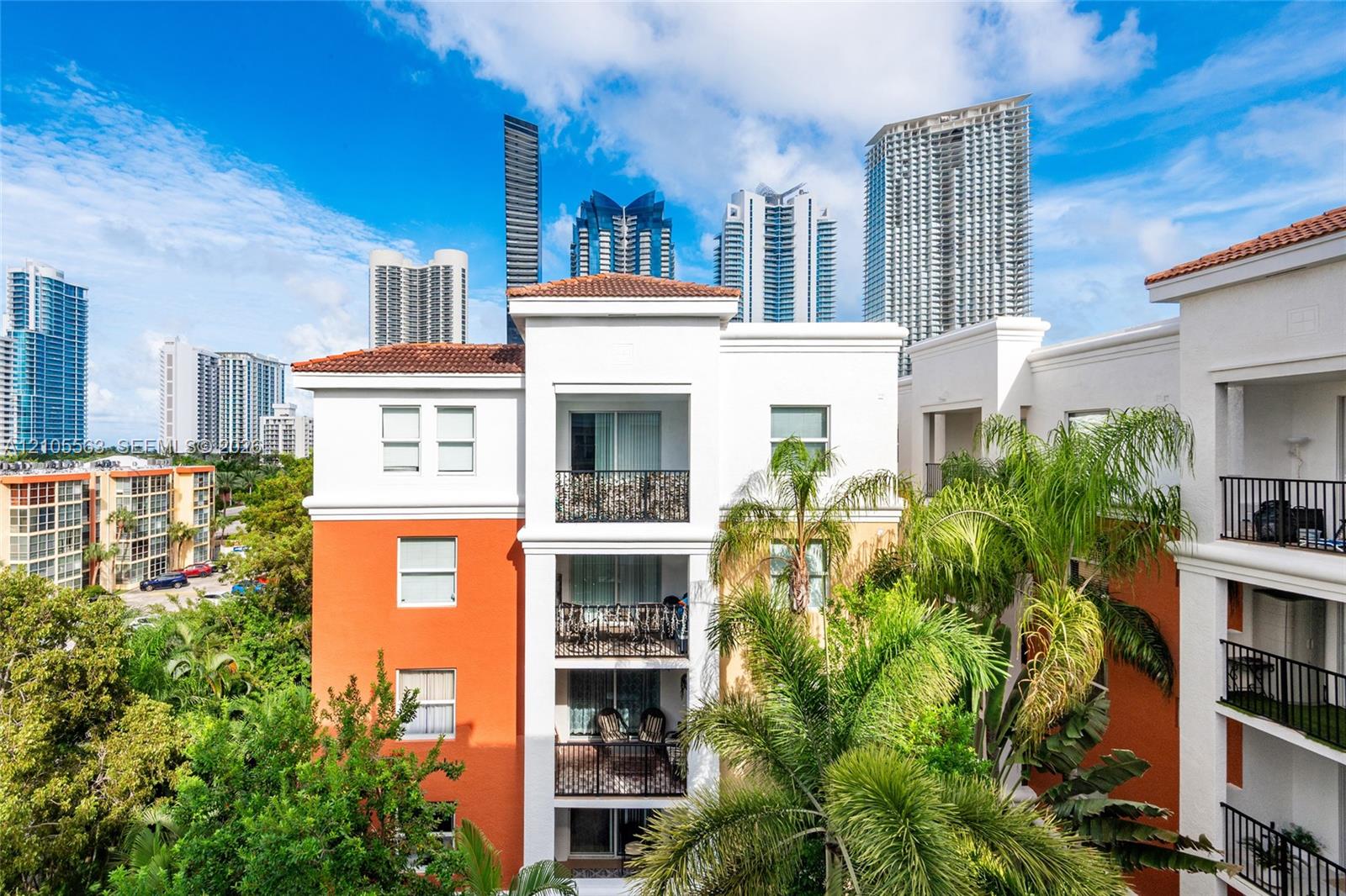 Multi-story building with white and orange exterior, tile roof accents, and multiple balconies featuring black wrought iron railings